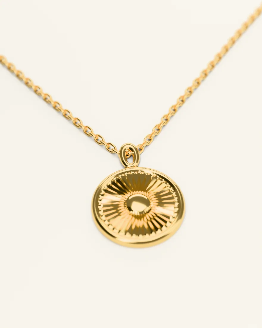 Round gold medallion with engraved rays on a fine chain