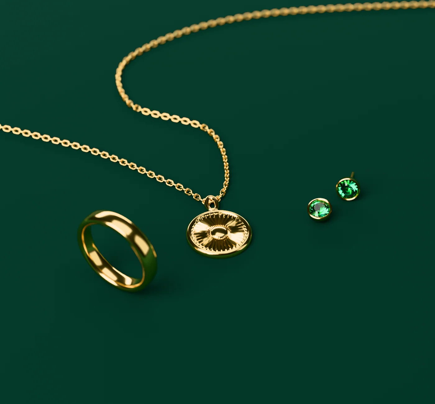 A sunburst medallion on a fine chain, a plain gold band and a pair of emerald studs on green velvet